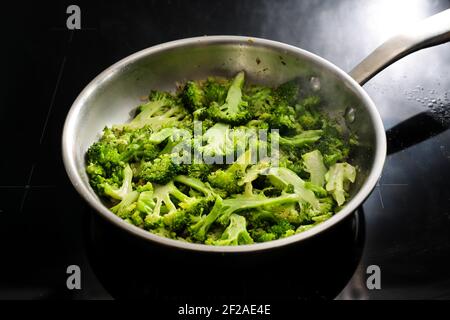 Brokkoli-Scheiben in einer Edelstahl-Bratpfanne auf einem schwarzen Herd, gesundes Kochen mit frischem Bio-Gemüse, ausgewählter Fokus, enge Schärfentiefe Stockfoto