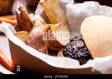 Ethisch angehobener Schweinefleischburger mit handgeschnittenen roten Kartoffelkeilen Und Gemüsestöcke nehmen Stock Foto Stockfoto