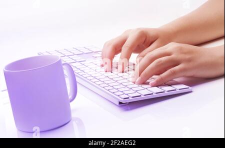Frau Hände tippen auf eine Tastatur und eine Tasse Kaffee vor weißem Hintergrund. Farbenfrohes Motiv. Weiche Kontrastfarben. Stockfoto