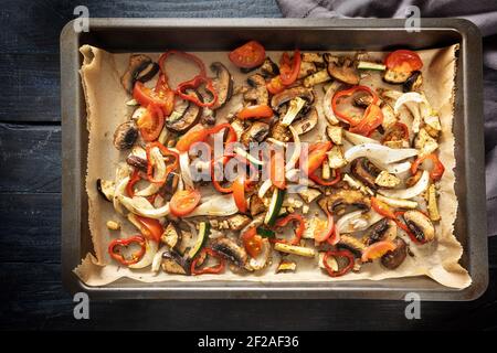 Ofengemüse wie Paprika, Tomate, Zucchini, Pilz, Fenchel und Auberginen auf einem Backblech auf dunklem rustikalem Holz, Hochwinkelansicht von oben, se Stockfoto