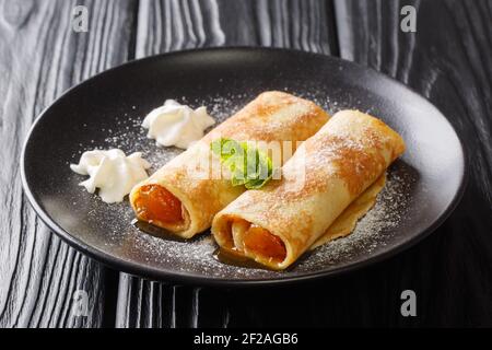 Portion leckere Crepes mit Aprikosenfüllung und Puderzucker in Nahaufnahme in einem Teller auf dem Tisch. Horizontal Stockfoto