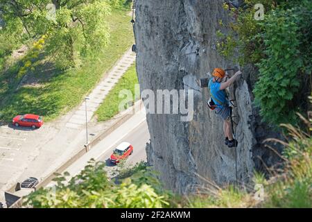 Decin, Tschechische Republik - Mai 7 2020: Erfahrener starker Mann auf Klettersteig klettern steilen Felswand über Straße Stockfoto