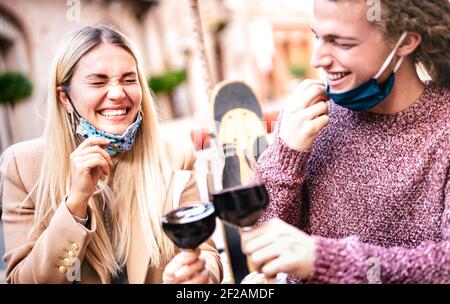 Junges Paar in der Liebe tragen offene Gesichtsmasken und mit Spaß an der Weinbar im Freien - Happy Hipster Liebhaber toasten Wein auf der Restaurantterrasse Stockfoto