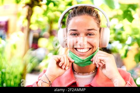 Junge Frau lächelnd Blick auf die Kamera mit offener Gesichtsmaske Und Kopfhörer - Neue normale Lifestyle-Konzept mit Millenial Mädchen Spaß im Freien Stockfoto