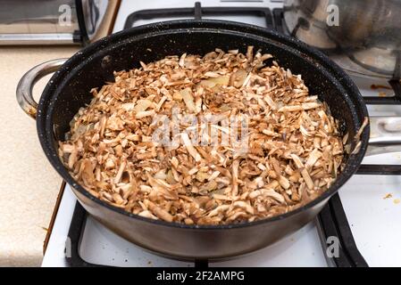 Rohe Pilze, in Streifen geschnitten, zum Braten in einer Pfanne zusammen mit Zwiebeln auf einem Gasherd vorbereitet. Stockfoto