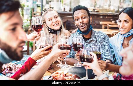 Menschen mit vielen Rassen, die im Restaurantgarten Wein toasten, tragen ein offenes Gesicht Maske - Neue normale Lifestyle-Konzept über glückliche Freunde haben Spaß zusammen Stockfoto