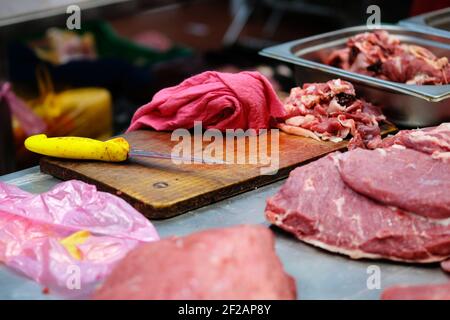 Theke des Verkäufers von frischem Fleisch auf dem lokalen Bauernmarkt. Holzschneidebrett, Messer, roter Lappen, Schweinefleisch, Rindfleisch, Behälter mit Fetzen. Stockfoto