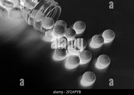 Pillen und Tabletten verschüttet aus der Glas-Pille-Flasche Auf schwarz glänzend geheimnisvollen Hintergrund Stockfoto
