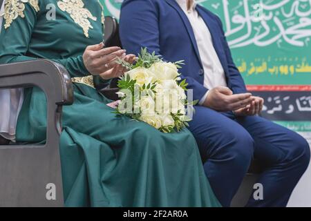 Nikah ist eine muslimische Hochzeitszeremonie. Braut und Bräutigam sitzen nebeneinander, die Hände im Gebet gefaltet. Ein Strauß Rosen liegt auf dem Schoß des Mädchens. Stockfoto