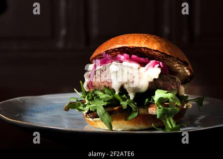 Frischer, appetitlich schmeckender Cheeseburger aus Rind mit Rucola und roten eingelegten Zwiebeln Auf einem hausgemachten Brötchen Stockfoto