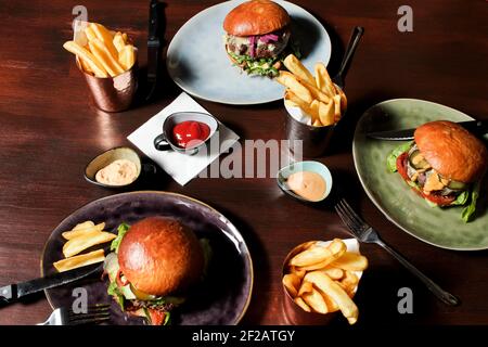 Verschiedene Burger auf dem Tisch, serviert frenc Pommes und Saucen auf Tellern. Nahaufnahme, Draufsicht. Stockfoto
