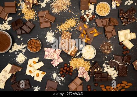 Viele verschiedene Arten von Schokolade und verschiedene Zutaten wie Nüsse und Kakaopulver liegen auf einem schwarzen Holzteller Foto von oben aufgenommen Stockfoto