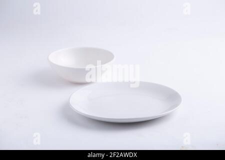 Weiße Tischwaren, verschiedene Formen einer leeren weißen Keramikschale und Platte auf einem weißen strukturierten Hintergrund angeordnet. Stockfoto