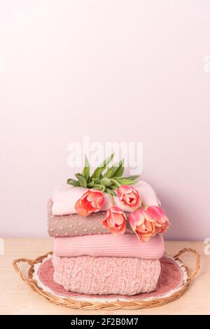 Ein Stapel Damen Strickpullover auf einem Weidentablett auf einem Regal, neben einem Blumenstrauß Stockfoto