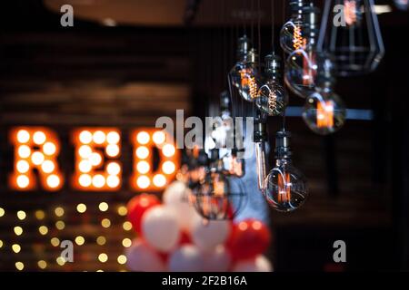 Dunkles Interieur mit vielen LED-Lampen und dekorativen Beleuchtungselementen in Form des Wortes "Rot". Rote und weiße Ballons. Stockfoto