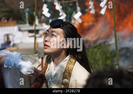 Hübsche weibliche buddhistische Pilgerin, die am Hiwatari Matsuri - Fire Walking Festival teilnimmt, während das Feuer hinter ihr brennt, Berg Takao, Hachioji, Japan Stockfoto