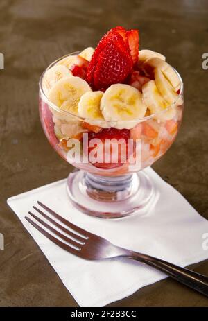Obstsalat auf einem Glas mit Papierserviette und Gabel auf Steingrund. Stockfoto