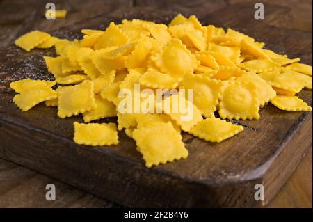 Tartollini mit Käse oder Fleisch zum Kochen in Brühe, traditionelles Gericht für Feiern in italien, Emilia Romagna Region. Frische hausgemachte Pasta mit Füllung auf einem Holztisch. Stockfoto