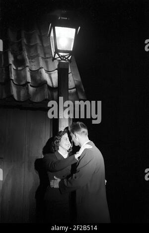 Liebe in der 1950s. Ein junges Paar steht am Abend unter einer Straßenlaterne und küsst sich. Schweden 1953 Ref. Pärm 1 Stockfoto