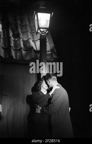 Liebe in der 1950s. Ein junges Paar steht am Abend unter einer Straßenlaterne und küsst sich. Schweden 1953 Ref. Pärm 1 Stockfoto