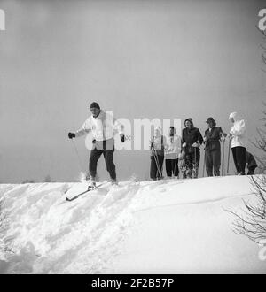 Winter in der 1940s. Eine Gruppe von Leuten beim Skifahren und bevor sie sich selbst beim Skifahren den Hügel hinunter versuchen, stehen sie und beobachten, wie es geht, wenn ein Mann sein Bestes versucht, ohne in den tiefen Schnee zu fallen. Schweden 1947. Kristoffersson Ref. AA30-9 Stockfoto