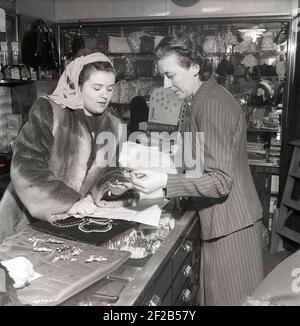 Einkaufen in der 1940s. Eine junge Frau in einem Geschäft, wo eine Verkaufsfrau präsentiert einige der Geschäfte Auswahl an Schmuck und Reize. Auf der Verkaufstheke sind Produkte aus Pond's Tissues zu sehen. Ein Produkt, das als das am nächsten zu einem feinen Taschentuch vermarktet wird, glatt, stark und saugfähig. Schweden 1947. Kristoffersson Ref. AB3-4 Stockfoto