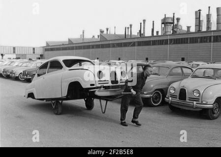 Automobilherstellung im Jahr 1950s. Die Saab Autofabrik in Trollhättan Schweden mit ihrer Produktionslinie. Ein seltsames Bild eines Arbeiters, der den Chassi eines Saab-Motorwagens auf einem Wagen hinter sich herschleppt. Das Modell ist Saab 96, das zwischen 1960-1963 hergestellt wurde. Schweden 1961 Stockfoto