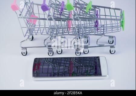 Handy vor drei Mini-Einkaufswagen als Ein Konzept für Online-Shopping Stockfoto