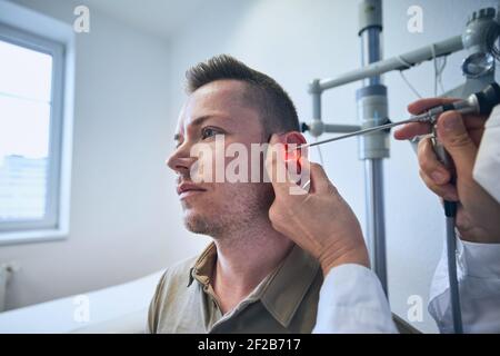 Patient in der HNO-Klinik. Facharzt - Otolaryngologe, der Ohrenuntersuchung des jungen Mannes macht. Stockfoto