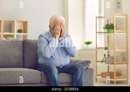 Älterer Mann bedeckt das Gesicht mit Händen und weint, trauert oder leidet unter Kopfschmerzen Stockfoto