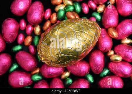 Stapel oder Gruppe von mehrfarbigen und verschiedenen Größen von bunten Folie verpackt Schokolade ostereier in rosa, rot, Gold und Limettengrün. Stockfoto