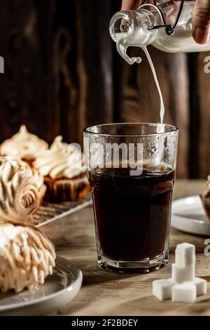 Milch in ein Glas heißen Kaffee gießen. Stockfoto