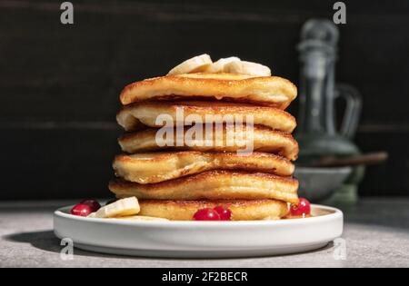 Teller mit frisch gebackenen Pfannkuchen auf Küchentisch dekoriert mit Banane und Beeren Stockfoto