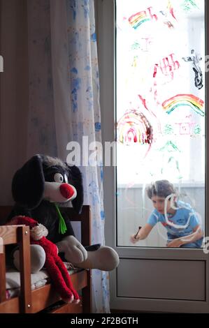 Plüsch Kaninchen Spione auf einem Jungen, der einen Regenbogen, Abstraktion und ein Haus auf dem Glasfenster zeichnet Stockfoto