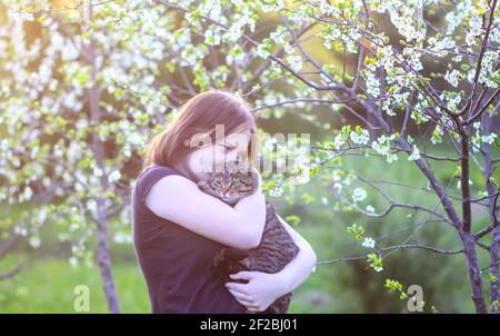 Das Mädchen hält in den Händen ihre schöne gestreifte graue Katze Im Freien auf Frühling Natur Hintergrund Stockfoto