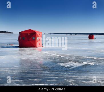 Barrie, Ontario, Kanada - 7. März 2021: Rotes Eis-Angelzelt mit Bohrmaschine auf gefrorenem blauem Eis der Kempenfelt Bay am Lake Simcoe im Winter Stockfoto