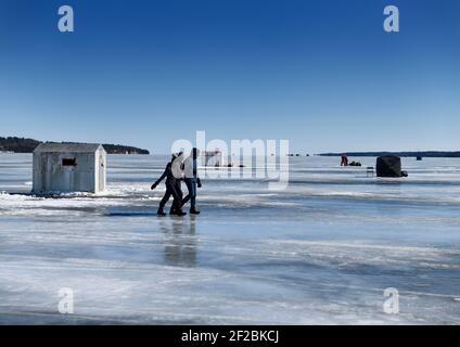 Blaues Eis und Himmel in Kempenfelt Bay of Lake Simcoe mit Eisfischen Hütten und Menschen zu Fuß auf Eis Barrie, Ontario, Kanada - 7. März 2021 Stockfoto