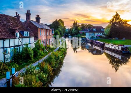 Die Sonne untergeht über Schmalbooten, die an einem Sommerabend auf dem Kennet- und Avon-Kanal im Zentrum der Stadt Hungerford, England, festgemacht sind Stockfoto