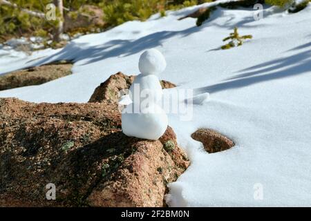 Schneemann sitzt auf einem Felsbrocken neben einem verschneiten Pfad zwischen den Pinien im Rocky Mountain National Park, Colorado Stockfoto