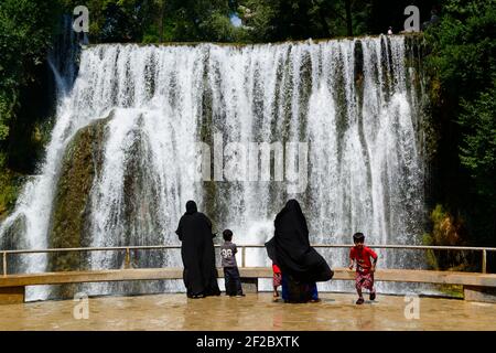 Zwei Frauen in schwarzem Tschador mit ihren Kindern machen Fotos von den 22 Meter hohen Pliva Wasserfällen in Jajce, Bosnien und Herzegowina. Kaskade Stockfoto