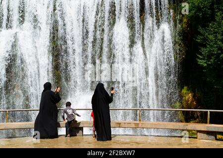 Zwei Frauen in schwarzem Tschador mit ihren Kindern machen Fotos von den 22 Meter hohen Pliva Wasserfällen in Jajce, Bosnien und Herzegowina. Kaskade Stockfoto