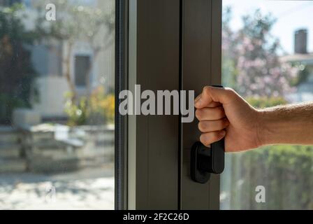 Hand halten Aluminium Fenstergriff Nahaufnahme. Der Mann öffnet oder schließt die Metall- oder PVC-Tür. Energieeffizient, Sicherheitsprofil, Blur Garten im Freien b Stockfoto