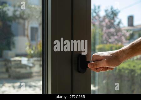 Hand halten Aluminium Fenstergriff Nahaufnahme. Der Mann öffnet oder schließt die Metall- oder PVC-Tür. Energieeffizient, Sicherheitsprofil, Blur Garten im Freien b Stockfoto