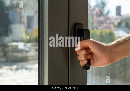 Der Mann öffnet oder schließt die Metall- oder PVC-Tür. Hand halten Aluminium Fenstergriff Nahaufnahme. Energieeffizient, Sicherheitsprofil, Blur Garten im Freien b Stockfoto