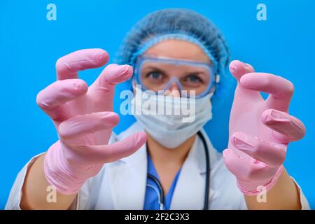 Der Arzt Hände mit bösen Augen greifen nach dem Patienten, blauer Hintergrund. Die Krankenschwester greift Sie in medizinischen Handschuhen, Nahaufnahme. Konzept zu Hause bleiben. Stockfoto