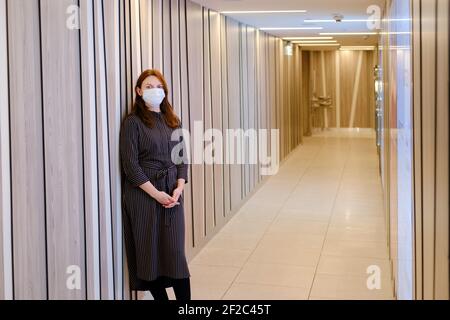 Rothaarige Frau in der Krankenhauslobby mit einer medizinischen Maske Auf ihrem Gesicht Stockfoto