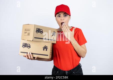 Junge schöne Frau trägt Kurier Uniform halten Lieferpakete schockiert Abdeckung Mund mit Hand für Fehler. Secret Konzept. Stockfoto