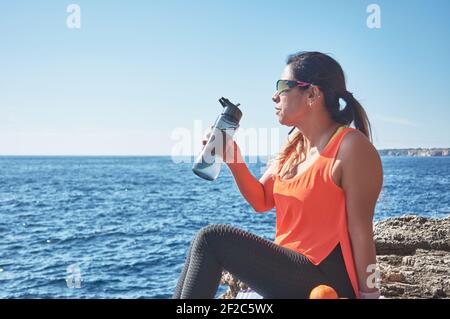 Lateinische Frau, mittleren Alters, ausruhen, Kraft zurückgewinnen, essen, Trinkwasser, nach einem Fitness-Studio-Sitzung, Kalorien zu verbrennen, fit zu halten, im Freien am Meer Stockfoto