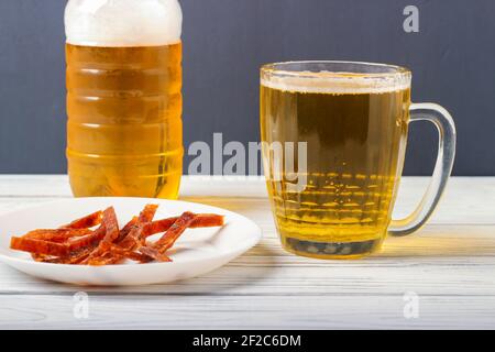 Bier in einem Becher auf dem Tisch und Scheiben Getrockneter gesalzener Fisch auf einer Platte Stockfoto