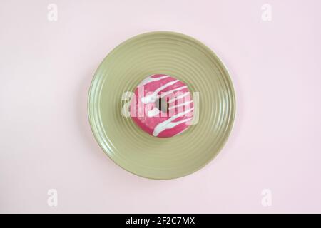 Ein leckerer rosa glasierte Donut auf beige runder Platte auf rosa Hintergrund. Draufsicht auf appetitlichen Donut. Nahaufnahme. Speicherplatz kopieren. Selektiver Fokus. Stockfoto